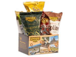 varied unique snacks products in a box with a light wood pattern, varied pictures of unique snacks factories and buildings, different kinds of pretzels surrounding it, and the unique snacks logo in the upper lefthand corner
