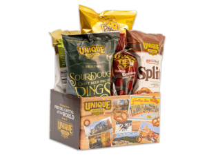 varied unique snacks products in a box with a light wood pattern, varied pictures of unique snacks factories and buildings, different kinds of pretzels surrounding it, and the unique snacks logo in the upper lefthand corner