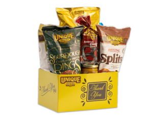 Thank you yellow basket box with a black square that has thank you written in yellow cursive and swirls and leaves surround the square with the unique snacks logo in the upper lefthand corner, filled with various Unique Snacks products